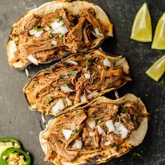 three pulled pork tacos with onions and cilantro on a black surface next to sliced jalapenos