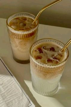 two glasses filled with liquid sitting on top of a table next to an open book