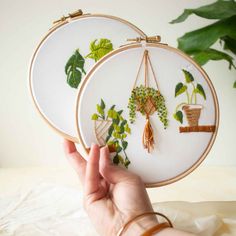 someone is holding up two embroidery hoops with plants on them