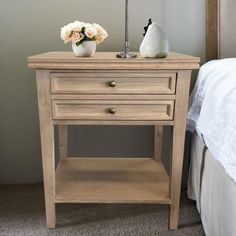 a nightstand with two flowers on it next to a bed