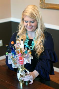 a woman sitting at a table holding a vase filled with bottles and condiments