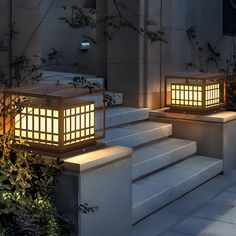 two lit up lanterns sitting on steps in front of a building with plants and bushes