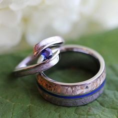 two wedding rings sitting on top of a green leaf next to a white and blue flower