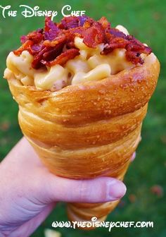 a hand holding an ice cream cone filled with macaroni and cheese covered in bacon