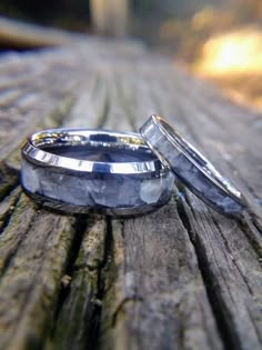 two wedding bands sitting next to each other on a piece of wood with trees in the background