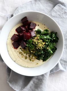 a white bowl filled with food sitting on top of a table next to a napkin