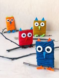 four little owls made out of yarn sitting on top of a white table next to sticks