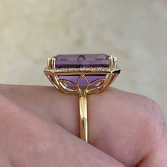 This beautiful gemstone ring centers an emerald cut, 12.50 carat, lively natural amethyst. Surrounding the gemstone is a halo of brilliant round diamonds that create a shared prong setting. The total diamond weight on this ring is approximately 0.42 carats. The mounting is handcrafted in 18k yellow gold and features a floral openwork under-gallery.
The measurements of this ring, including the halo, are approximately 19.04mm x 15.21mm.
This ring can be resized to any finger size at no additional cost.
If you have any questions regarding the Manorville ring, please feel free to contact us. Luxury Yellow Gold Amethyst Ring With Emerald Cut, Luxury Emerald-cut Amethyst Ring For Formal Events, Luxury Emerald Cut Amethyst Ring For Formal Occasions, Luxury Amethyst Ring With Emerald Cut Diamond, Luxury Amethyst Ring With Halo Setting, Luxury Purple Amethyst Ring With Halo Setting, Luxury Amethyst Ring Emerald Cut, Luxury Emerald Cut Amethyst Ring With Diamond Setting, Luxury Emerald-cut Diamond Amethyst Ring