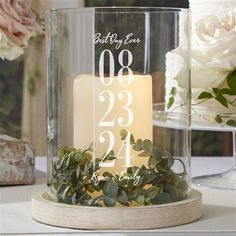 a candle that is sitting inside of a glass container on a table with flowers in the background