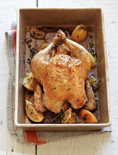 a roasted chicken in a roasting pan with vegetables