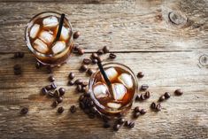 two glasses filled with ice and coffee beans on top of a wooden table next to each other