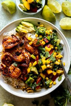 a white plate topped with shrimp, rice and veggies next to lime wedges