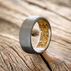 a wedding ring with gold inlays sits on top of a piece of wood