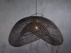 a light that is hanging from the ceiling in front of a concrete wall with a wire basket on it