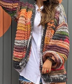 a woman wearing a multicolored cardigan sweater and denim shorts with her hands on her head