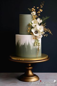 a three tiered cake with white flowers and greenery on top, sitting on a gold pedestal