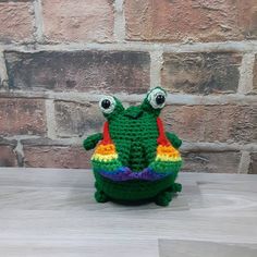 a crocheted frog sitting on top of a wooden table next to a brick wall