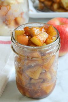 a jar filled with apple slices next to an apple and another bowl full of apples in the background