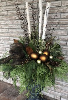 a vase filled with candles and greenery next to a brick wall