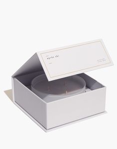 an open box with a candle inside it on a white surface, showing the lid