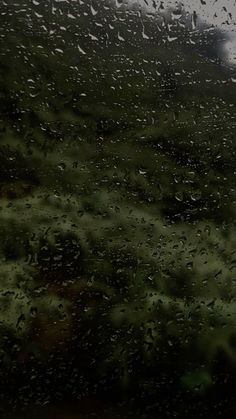 rain drops on the window as it is raining in an open field with green grass