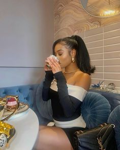 a woman sitting on a blue couch drinking from a glass in front of her face