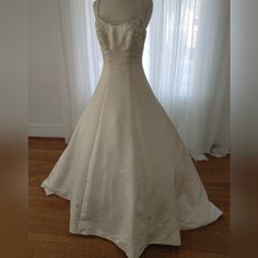 a wedding dress on display in front of a window with white curtains and wooden flooring