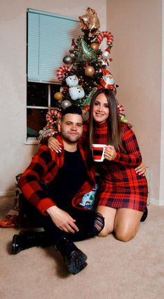 a man and woman are sitting in front of a christmas tree holding coffee mugs