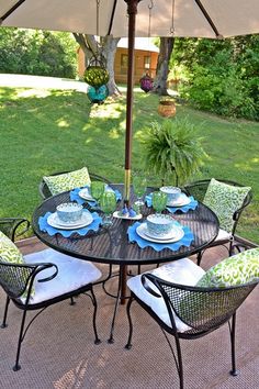 an outdoor table with chairs, plates and an umbrella over it in the middle of a yard