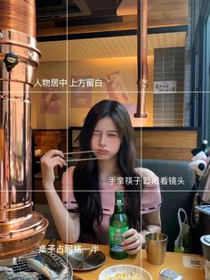 a woman sitting at a table with a beer in front of her and an advertisement on the wall behind her