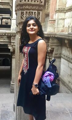 a woman standing in front of a building with a backpack on her shoulder and smiling at the camera