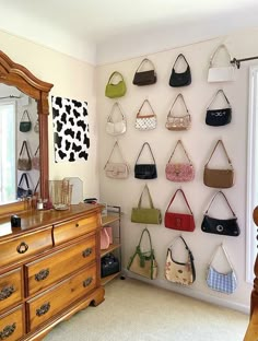 purses are hanging on the wall in front of a dresser with a large mirror