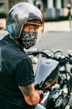 a man wearing a motorcycle helmet sitting on a motor bike in the street with his face covered by a bandana