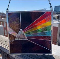 a colorful stained glass sun catcher hanging on a wooden fence with buildings in the background