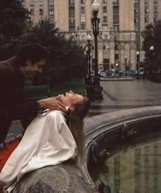 a woman laying on top of a rock next to a man in a black suit