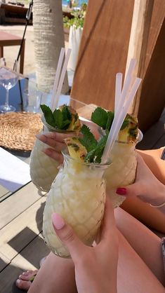 two people holding up drinks with strawberries and pineapple