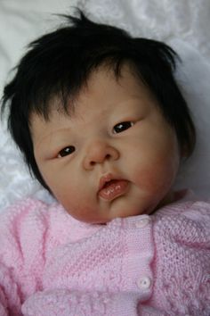 a baby doll with black hair laying on a white blanket and looking at the camera