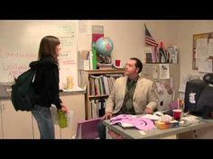 a woman standing next to a man sitting at a desk in an office area with bookshelves