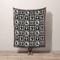 a woman standing in front of a wall holding up a black and white blanket with an abstract design