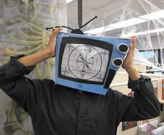 a man with a tv on his head in an office cubicle, holding up the television