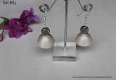 a pair of silver earrings sitting on top of a metal stand next to purple flowers