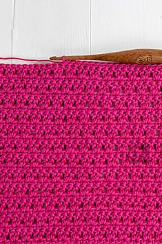 a pink crocheted purse with a wooden handle on a white surface next to a pair of scissors