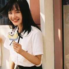 a woman standing next to a building holding a bird shaped object in her hand and smiling at the camera