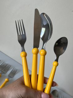 a person holding five forks and spoons in their hand, all with yellow handles