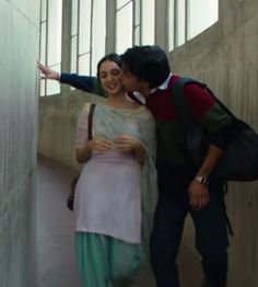 a man and woman standing next to each other near a wall with windows in the background