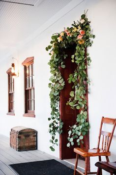 a wooden chair sitting in front of a doorway with plants growing on the outside wall