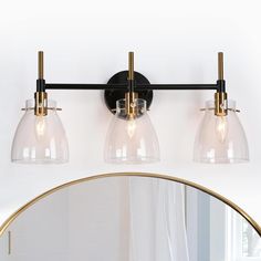 three light bathroom fixture with clear glass shades and gold accents on the wall above mirror