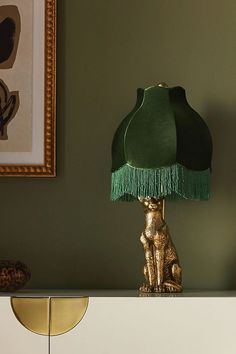 a green lamp sitting on top of a white dresser next to a painting and framed pictures