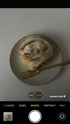 a white plate topped with a pastry covered in icing next to a golden fork