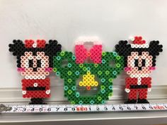 three mickey and minnie mouses made out of perler beads on a ruler in front of a white wall